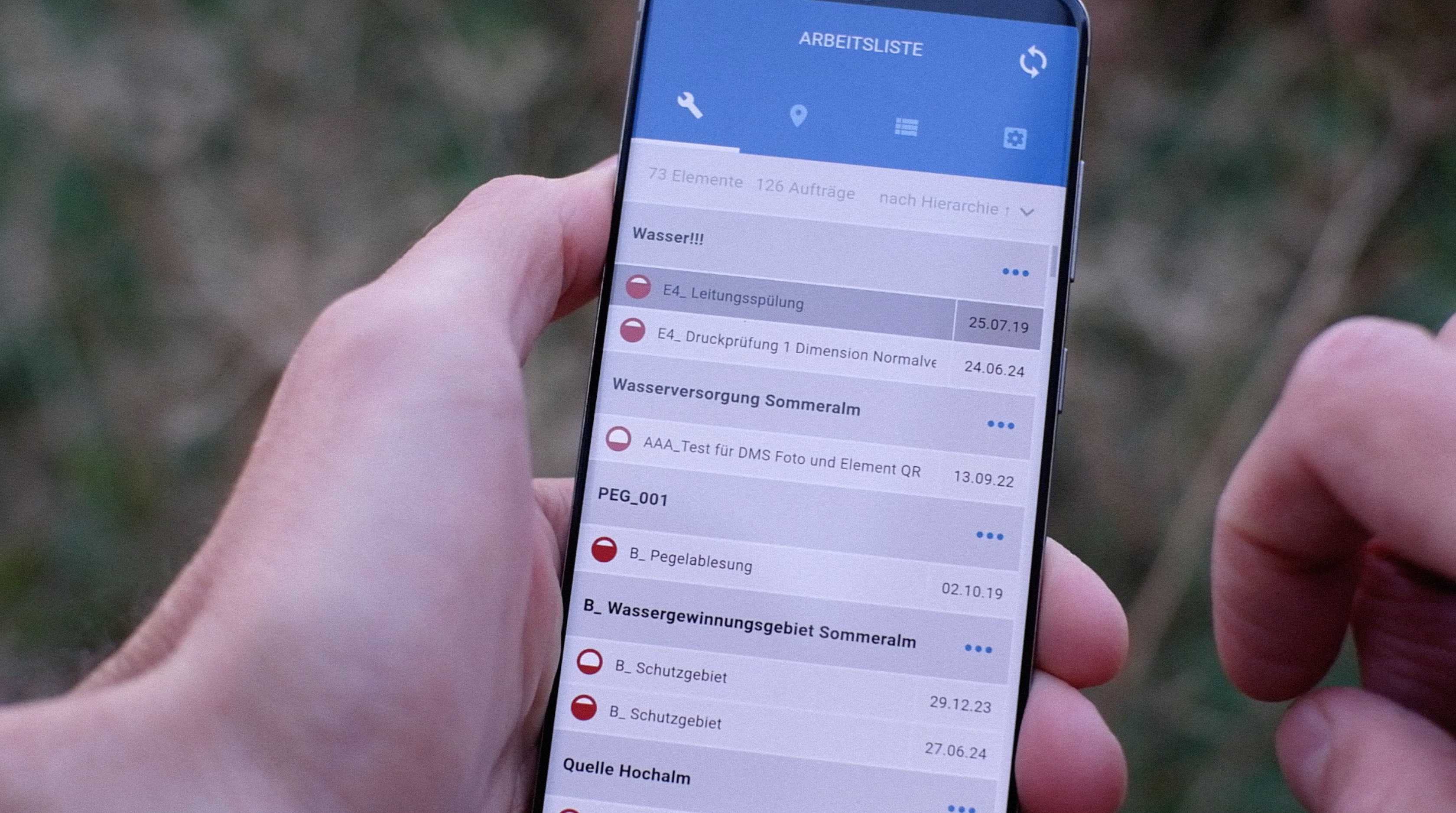 Hand holding smartphone. Screen displays list of technical elements.