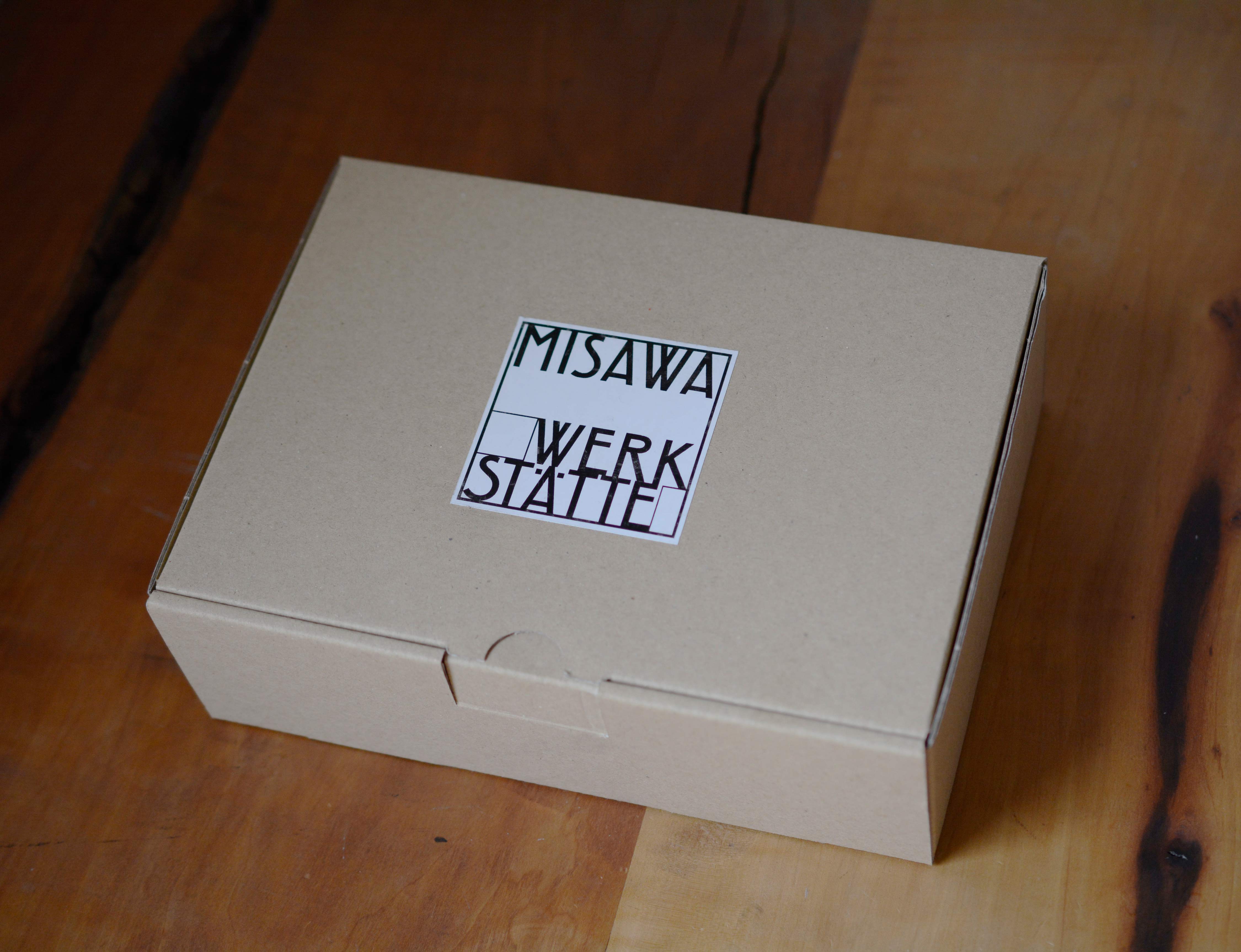 Brown carton box. White sticker with logo on top.
