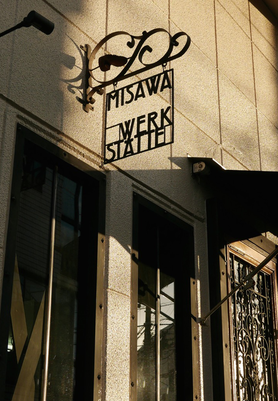 Business sign fixed on wall above shop windows. Thin iron frame with letters hangs down from iron rack.