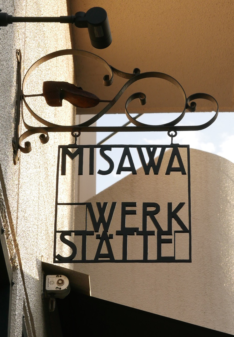 Business sign fixed on wall above shop windows. Thin iron frame with letters hangs down from iron rack.