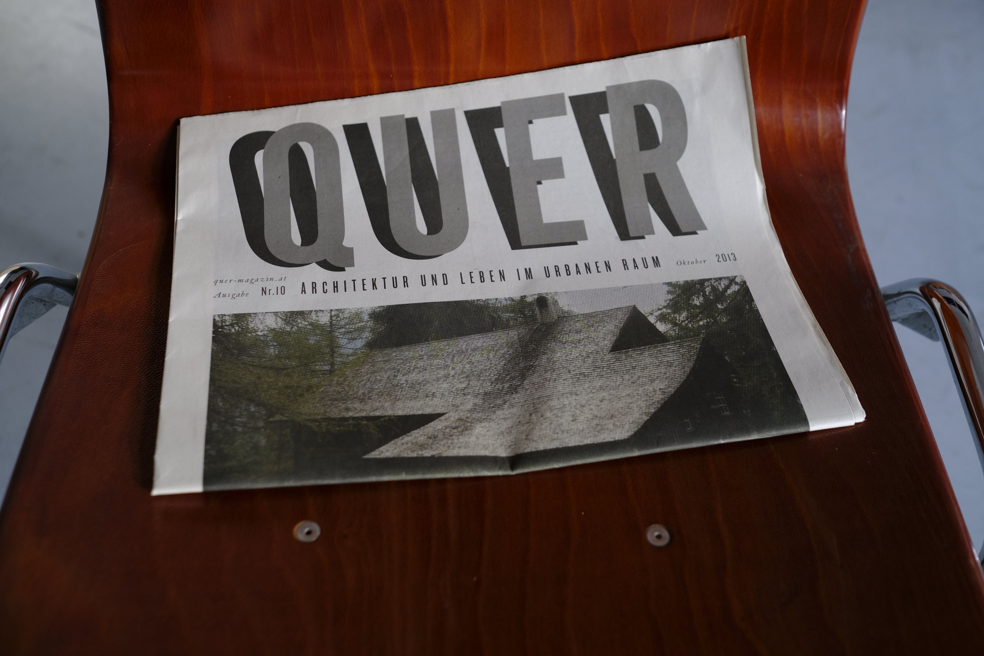 Folded newspaper on chair. Large title reads: Quer.