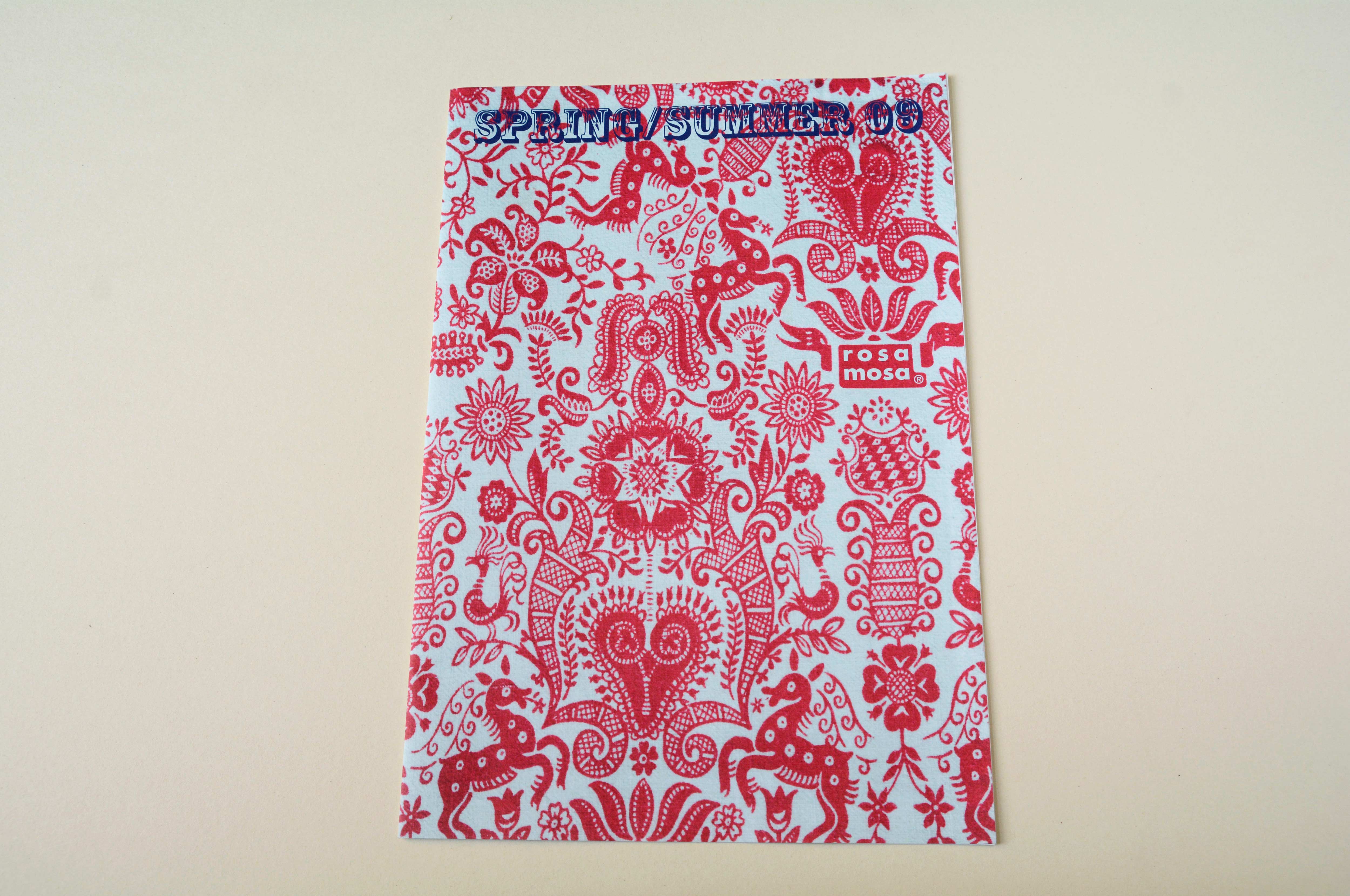 Lookbook cover front. Figurative pattern in red with incorporated logo. Blue title font overlayed.