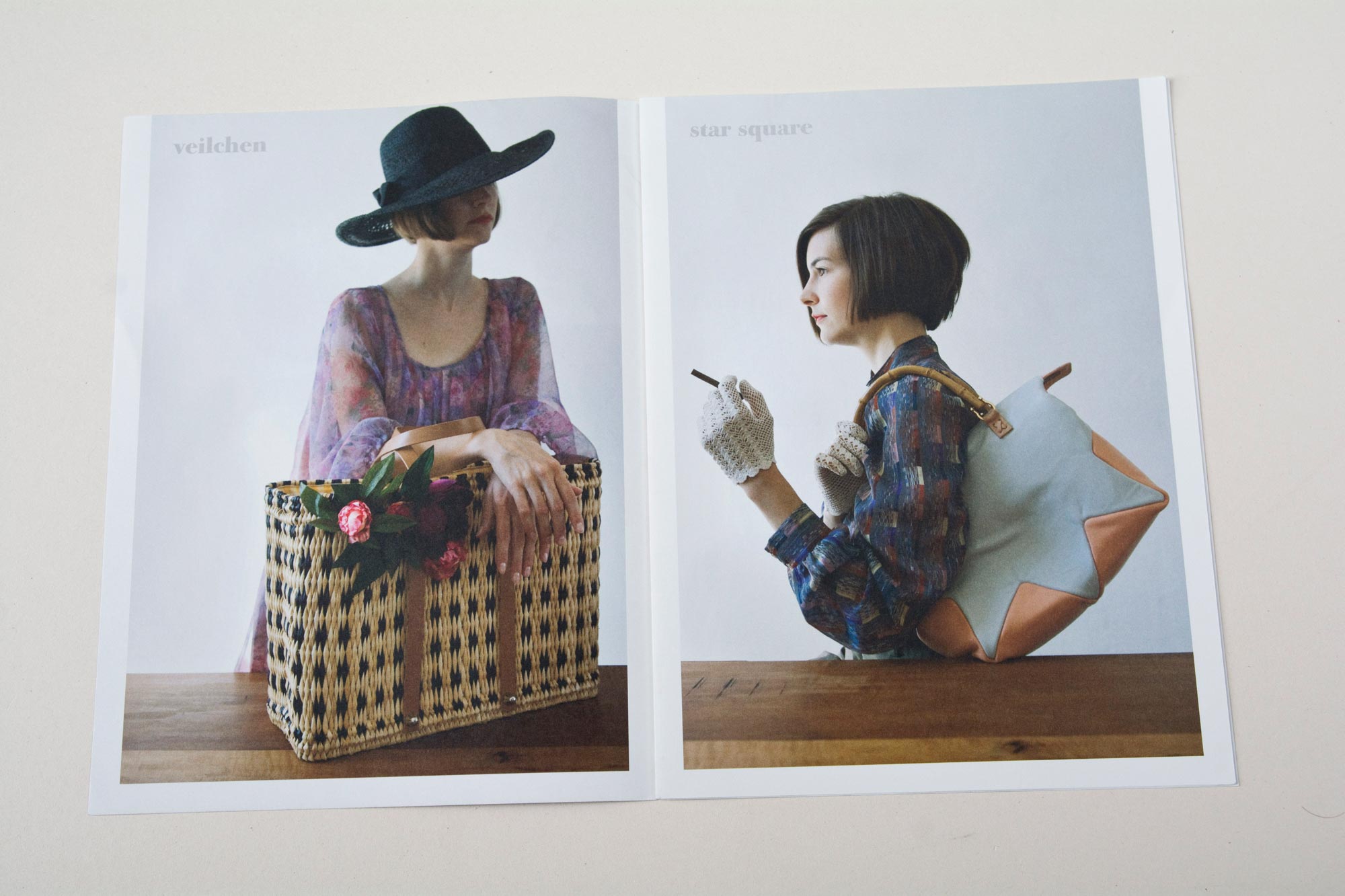 Double page. Left: Large handbag standing on wooden table. Woman behind with arms on it. Right: Woman sitting at wooden table. Wearing handbag on shoulder and holding cigarillo in hand.