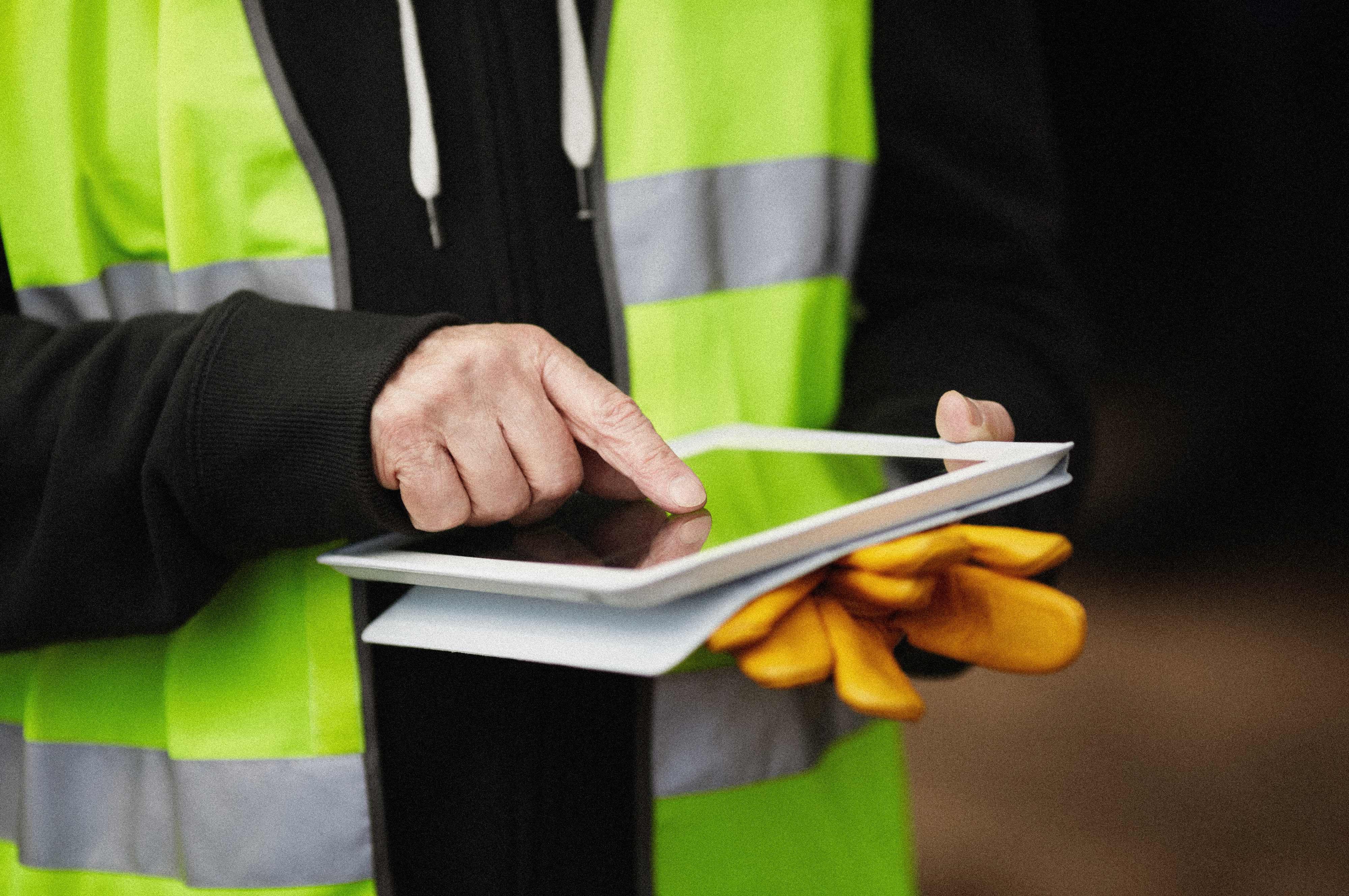 Person wearing flouroscent safety vest holding tablet in hands.
