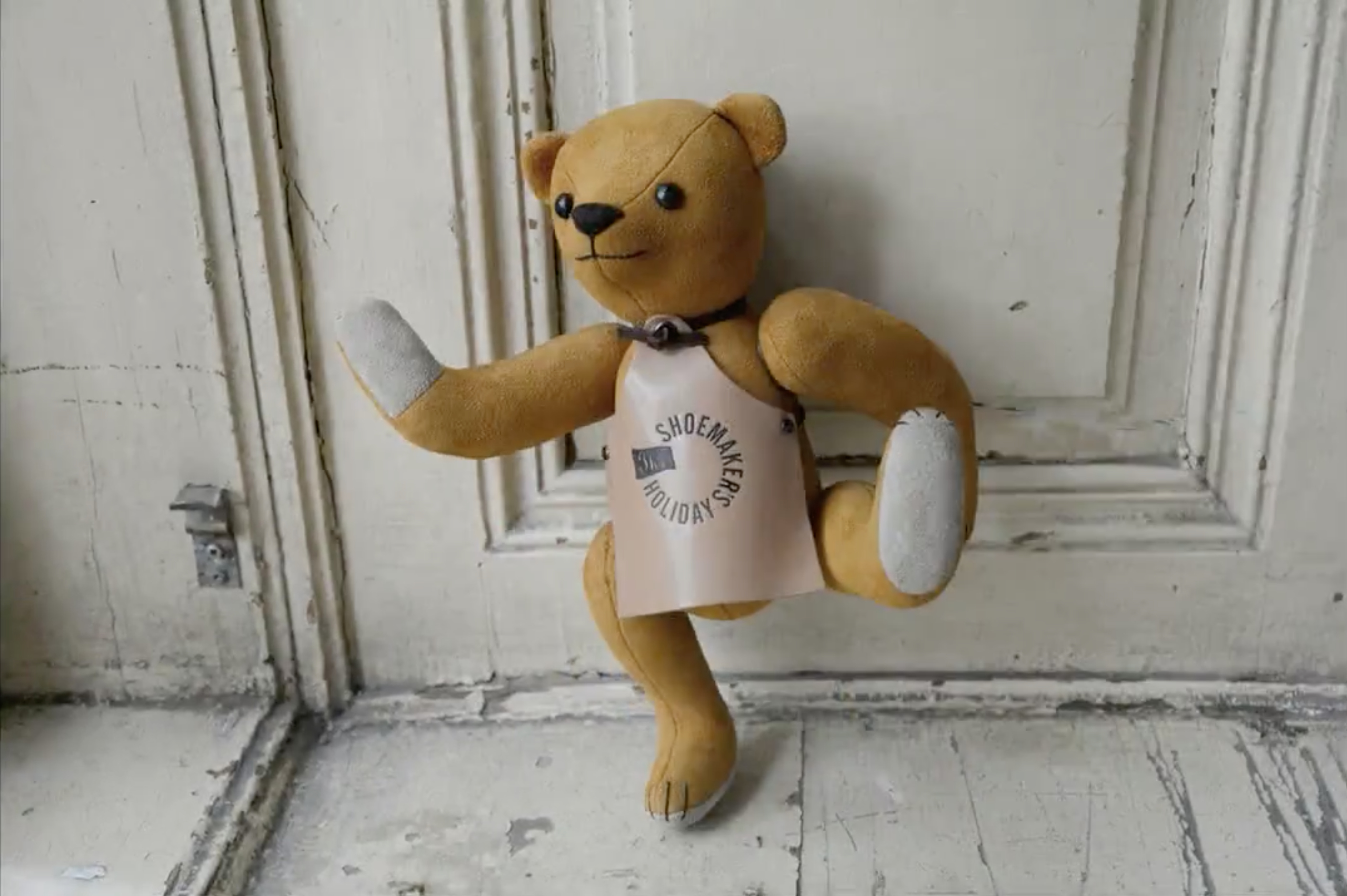 Teddybear in front of old wooden door. Wearing leather apron punched with logo.