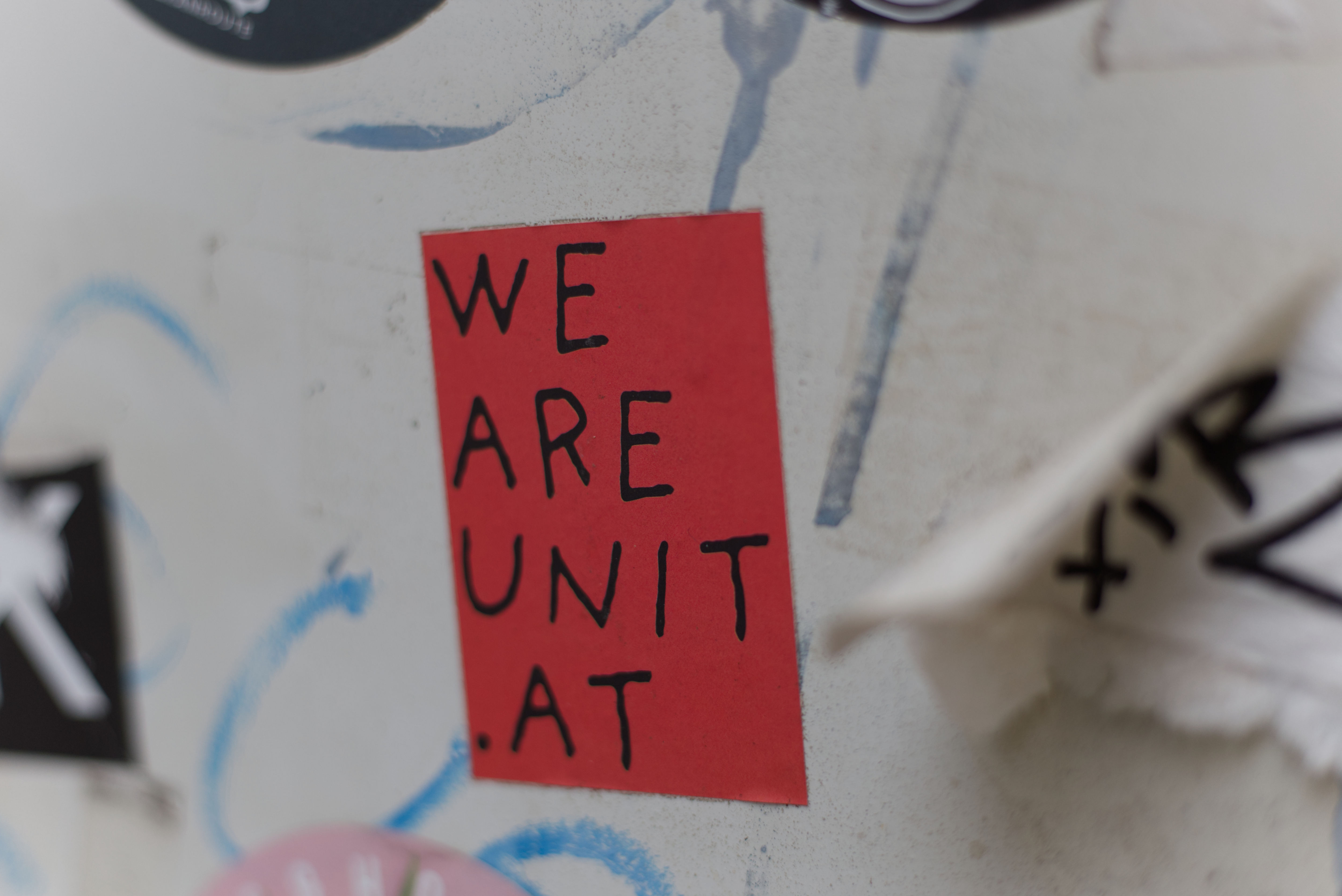 Close-up of sticker on the street. Written in loose script-font: weareunit.at