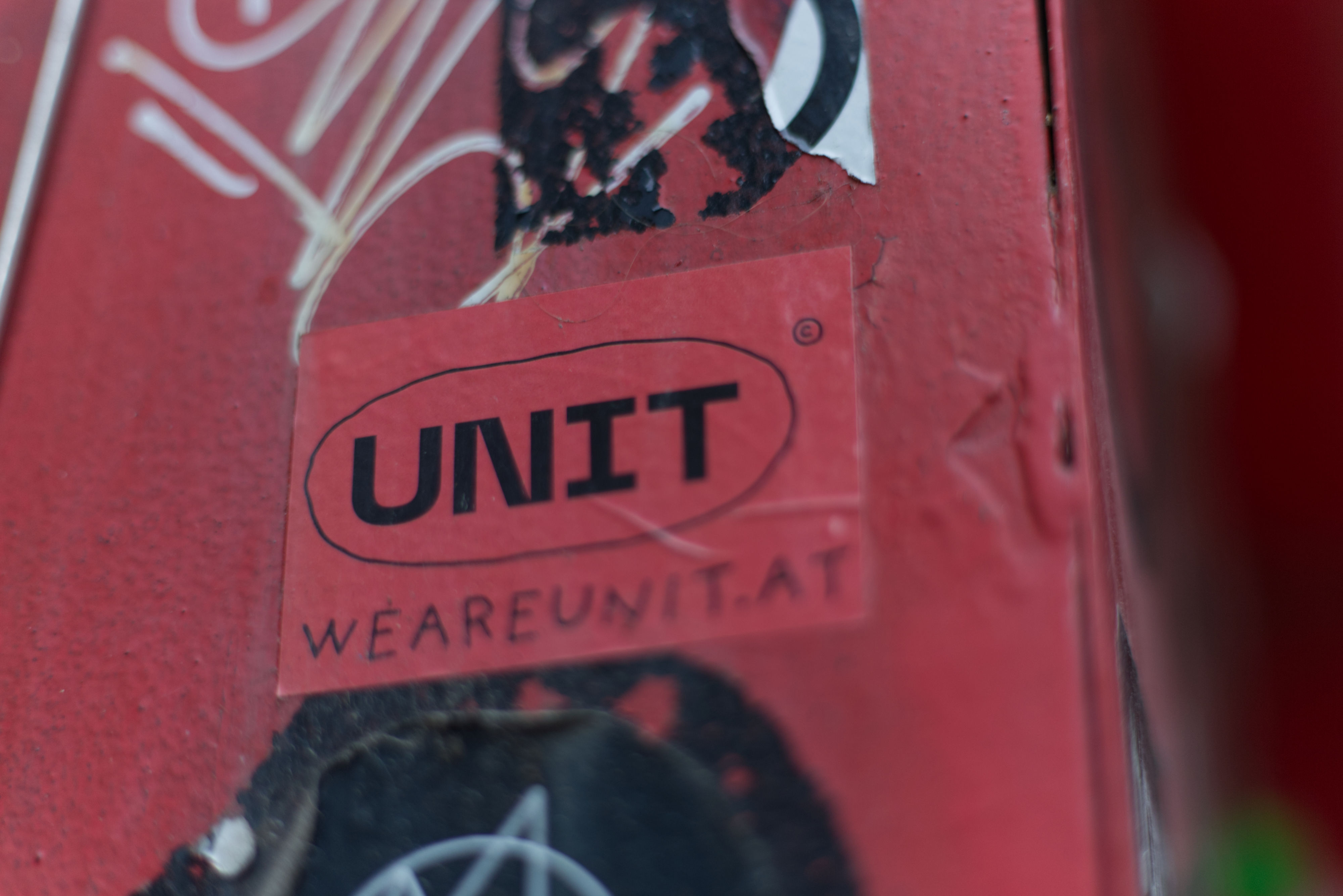 Close-up of sticker on the street. Written in loose script-font: weareunit.at